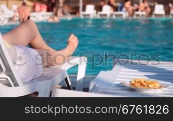 women&acute;s legs near the swimming pool with a plate of chips