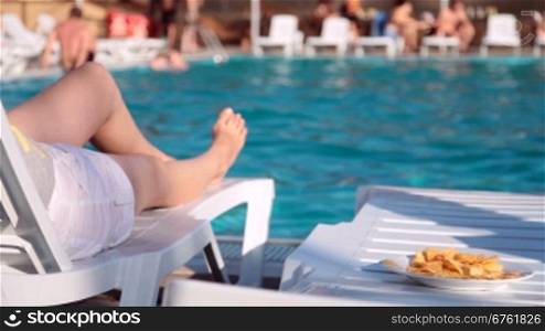 women&acute;s legs near the swimming pool with a plate of chips