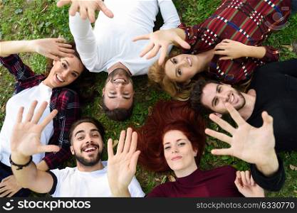 Women and men laying on grass wearing casual clothes. Group of young people together outdoors in urban park.
