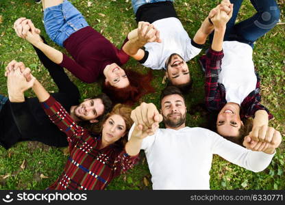 Women and men laying on grass wearing casual clothes. Group of young people together outdoors in urban park.