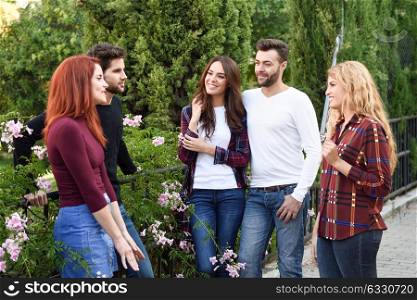 Women and men talking in the street wearing casual clothes. Group of young people together outdoors in urban background.