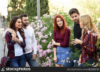 Women and men talking in the street wearing casual clothes. Group of young people together outdoors in urban background.