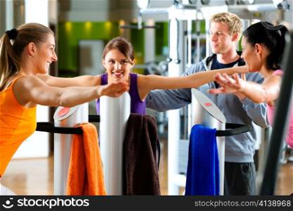 women and trainer in gym in front of a exercising machine doing fitness exercises