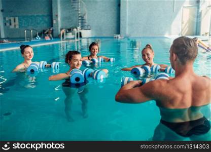 Women aqua aerobics traninig with dumbbells in indoor swimming pool. Female group with male trainer, water sport. Women aqua aerobics traninig with dumbbells