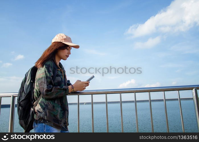 women asian with bright backpack looking at a map. View from back of the tourist traveler on background mountain, Female hands using smartphone,