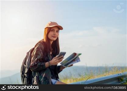 women asian with bright backpack looking at a map. View from back of the tourist traveler on background mountain, Female hands using smartphone, holding gadget