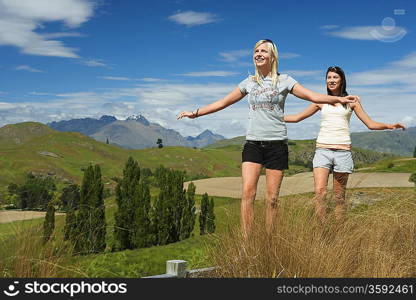 Women balancing on fence in field with mountains behind