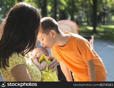 Women, brother and baby in a park. Child kissing baby