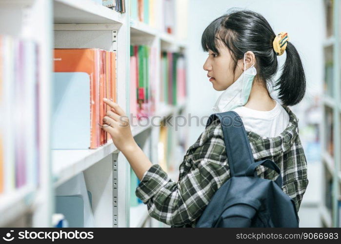 Women carrying a backpack and searching for books in the library.