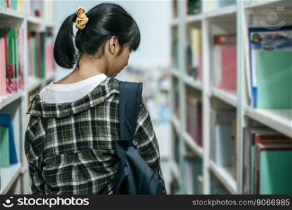 Women carrying a backpack and searching for books in the library.