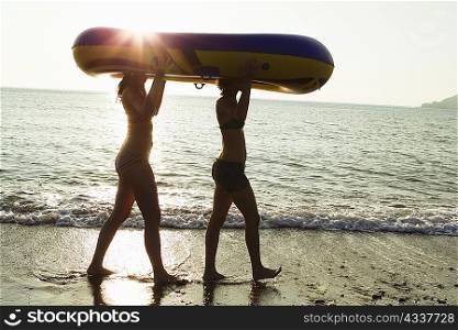Women carrying inflatable boat on beach