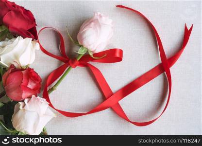 Women day image with a pink rose tied with a red ribbon in shape of the number 8, surrounded by red and white roses, on a vintage fabric background.