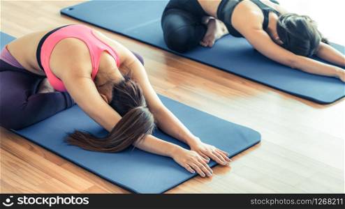 Women doing back stretching yoga pose, sitting on mat in fitness gym group class. Healthy lifestyle and wellness concept.