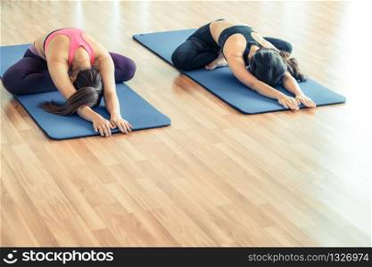 Women doing back stretching yoga pose, sitting on mat in fitness gym group class. Healthy lifestyle and wellness concept.