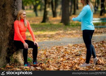 Women Exercising Outdoors in Public Park in the Fall. Trainer Looking at Woman Doing Squat Hold.. Women Exercising Outdoors in Public Park in the Fall.