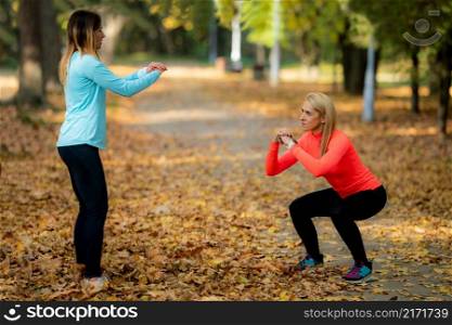 Women Exercising Outdoors in Public Park in the Fall. Trainer Looking at Woman Doing Squats.. Women Exercising Outdoors in Public Park in the Fall.