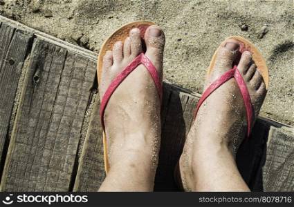 Women foots on the beach. Pink thongs. Wooden board