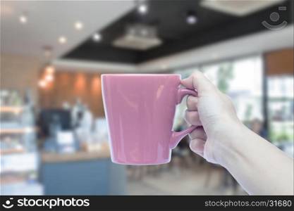 Women hand holding mug with blurred cafe interior for background