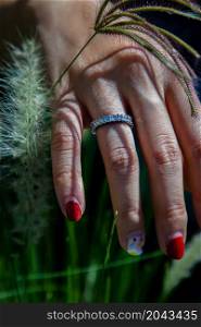Women hand. Sterling silver female ring on the fingers of a lady and red nail on sedge on a green meadow. Beauty and accessories, No focus, specifically.