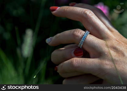 Women hand. Sterling silver female ring on the fingers of a lady and red nail on nature background. Beauty and accessories, No focus, specifically.