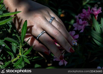 Women hand. Sterling silver female ring on the fingers of a lady and red nail on pink flower. Beauty and accessories, Selective focus.