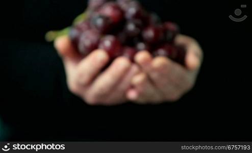 Women hands holding a nice fresh red grapes on a black background. DoF