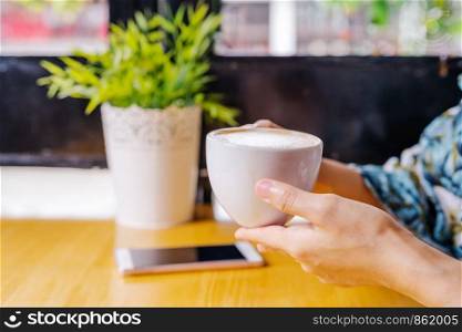 women hands holding hot cup of coffee or tea in morning sunlight