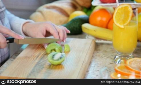 women hands preparing fruit salad slicing kiwi on chopping board