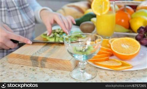 women hands preparing fruit salad slicing kiwi on chopping board