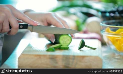 Women hands with knife cutting cucumber on board in kitchen