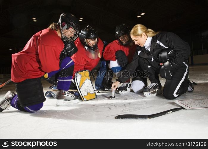 Women hockey players on ice looking at game plan with coach.