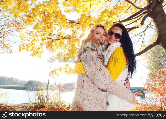 Women hug in autumn park. Two pretty young women hug in autumn park