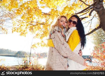 Women hug in autumn park. Two pretty young women hug in autumn park