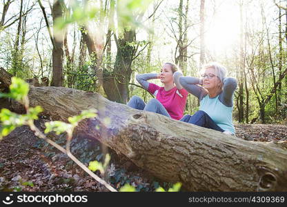 Women in forest hands behind head doing sit up against fallen tree