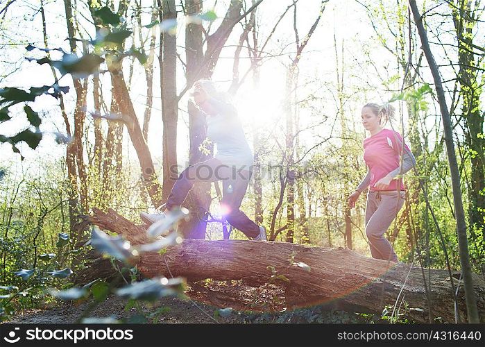 Women in forest jumping over fallen tree