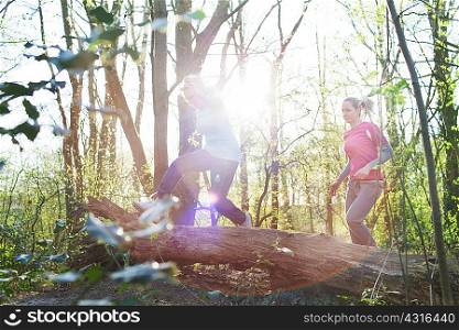 Women in forest jumping over fallen tree