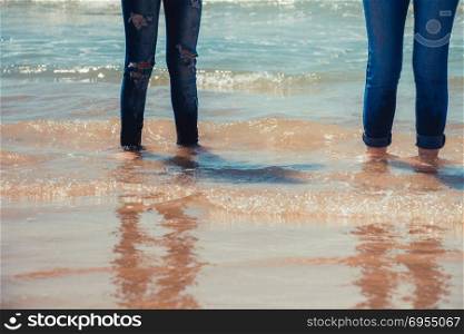 Women legs in blue jeans standing in the sea water on the coast.