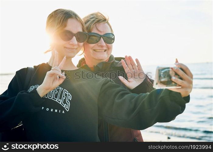 Women making gesture and waving during video call on smartphone during trip on summer vacation. Taking selfie photos