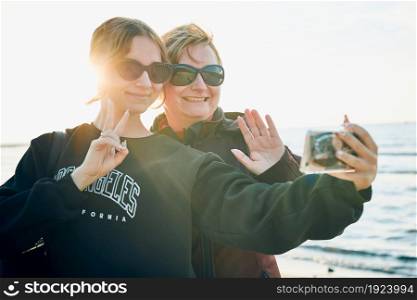 Women making gesture and waving during video call on smartphone during trip on summer vacation. Taking selfie photos