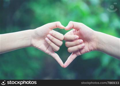 women making heart shapes with their hands on nature green background