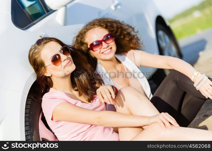 Women near car. Young pretty women sitting near white car at side of road