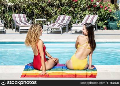 women of different ethnicities sitting at the edge of a pool on a gay pride flag.