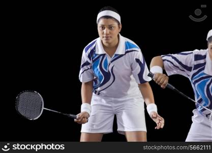 Women playing badminton doubles over black background