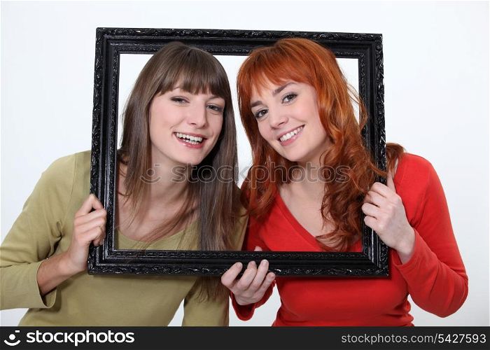 Women poking heads through empty picture frame
