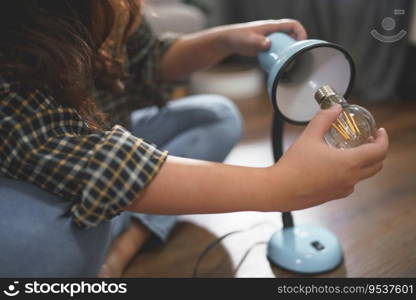 Women replacing the light bulb of desk lamp while assembling electronic equipment for new house.
