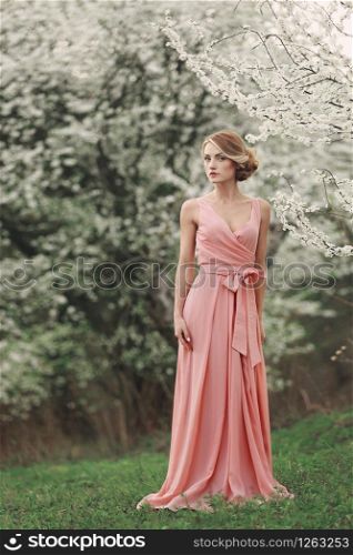 women&rsquo;s day. full length young stylish woman near blossoming tree in the spring park. blonde girl with hairstyle in pink dress. flowering trees background.. women&rsquo;s day. full length young stylish woman near blossoming tree in the spring park. blonde girl with hairstyle in pink dress. flowering trees background