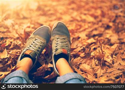 Women&rsquo;s feet over dry autumn leaves background, body part, woman sitting and relaxed on the ground in the autumnal forest in sunny day, enjoying weekend outdoors