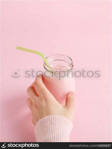 Women&rsquo;s hand taking glass bottle of fruit yogurt with straw. Pastel pink background with copy space. Healthy lifestyle concept, minimal, vertical.. Women&rsquo;s hand taking bottle of fruit yogurt on pink.