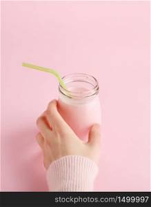 Women&rsquo;s hand taking glass bottle of fruit yogurt with straw. Pastel pink background with copy space. Healthy lifestyle concept, minimal, vertical.. Women&rsquo;s hand taking bottle of fruit yogurt on pink.