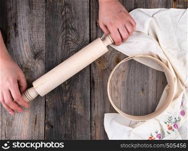 women's hands are holding an old wooden rolling pin on a gray table, a row of round sieve for flour, top view